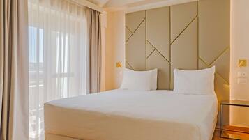 A hotel room with a large bed, a modern headboard, and a large window with curtains.