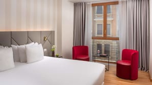 Een hotelkamer met een groot bed, twee rode stoelen, een kleine tafel met een boek en een open haard.