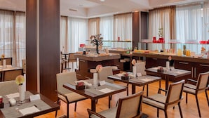 Een restaurantgedeelte in een hotel met meerdere tafels, stoelen en een buffet.