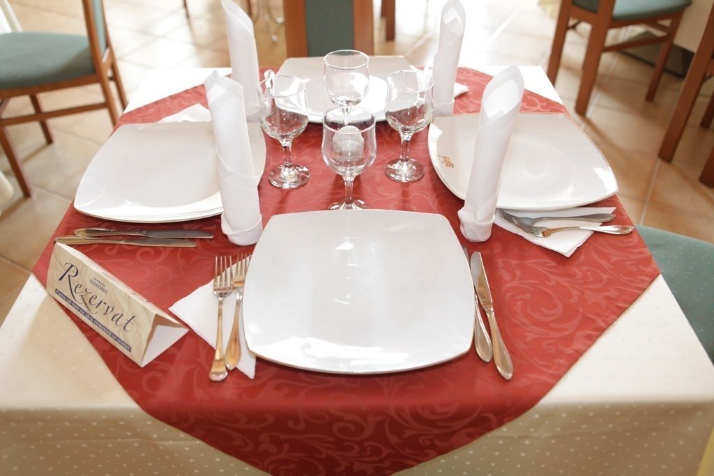 Una mesa preparada para cuatro con mantel rojo, platos blancos y cubiertos, y un letrero que dice 'Reservation'.