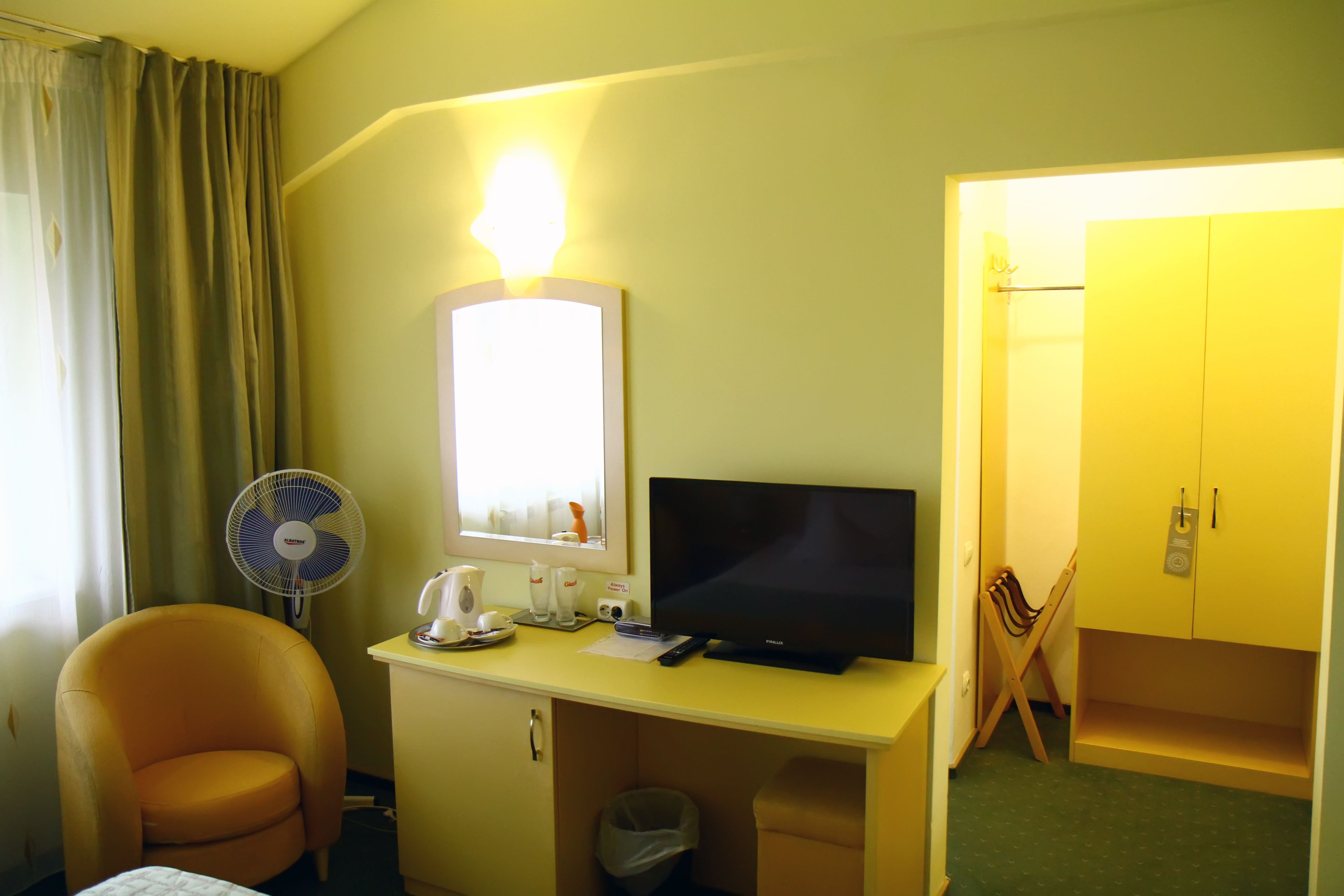 Habitación de hotel con escritorio, televisor, silla, ventilador, espejo y armario.