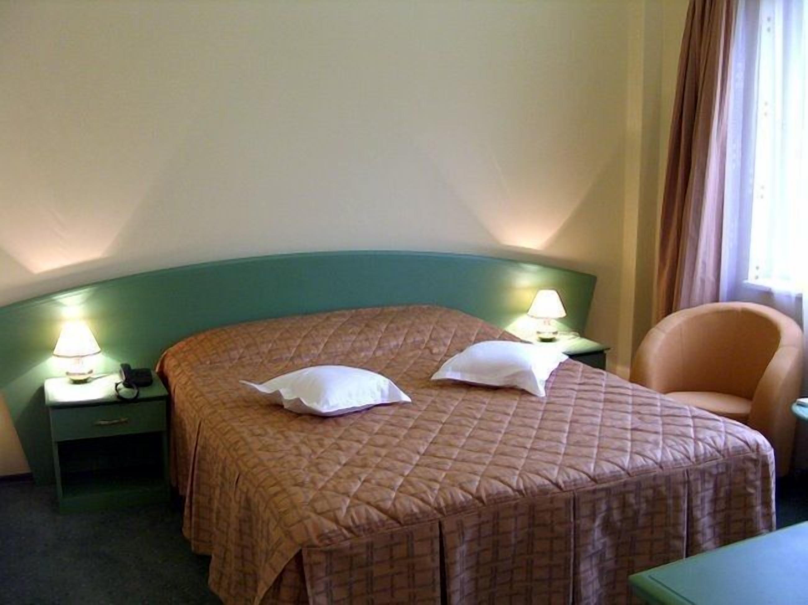 A hotel room with a large bed, two bedside lamps, a chair, and a nightstand.