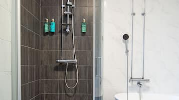 Un baño moderno con ducha acristalada, bañera independiente y paredes con azulejos oscuros.