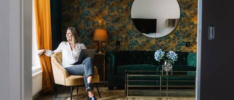 A room with a green sofa, a round mirror on the wall, and a laptop on a chair.
