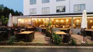 An outdoor cafe area with tables and chairs, a building with multiple windows, and a statue in the background. - Skara Konsthotell (Skara)