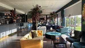 A spacious lobby with a bar area, seating arrangements, and large windows offering a view of the outdoors. - Skara Konsthotell (Skara)
