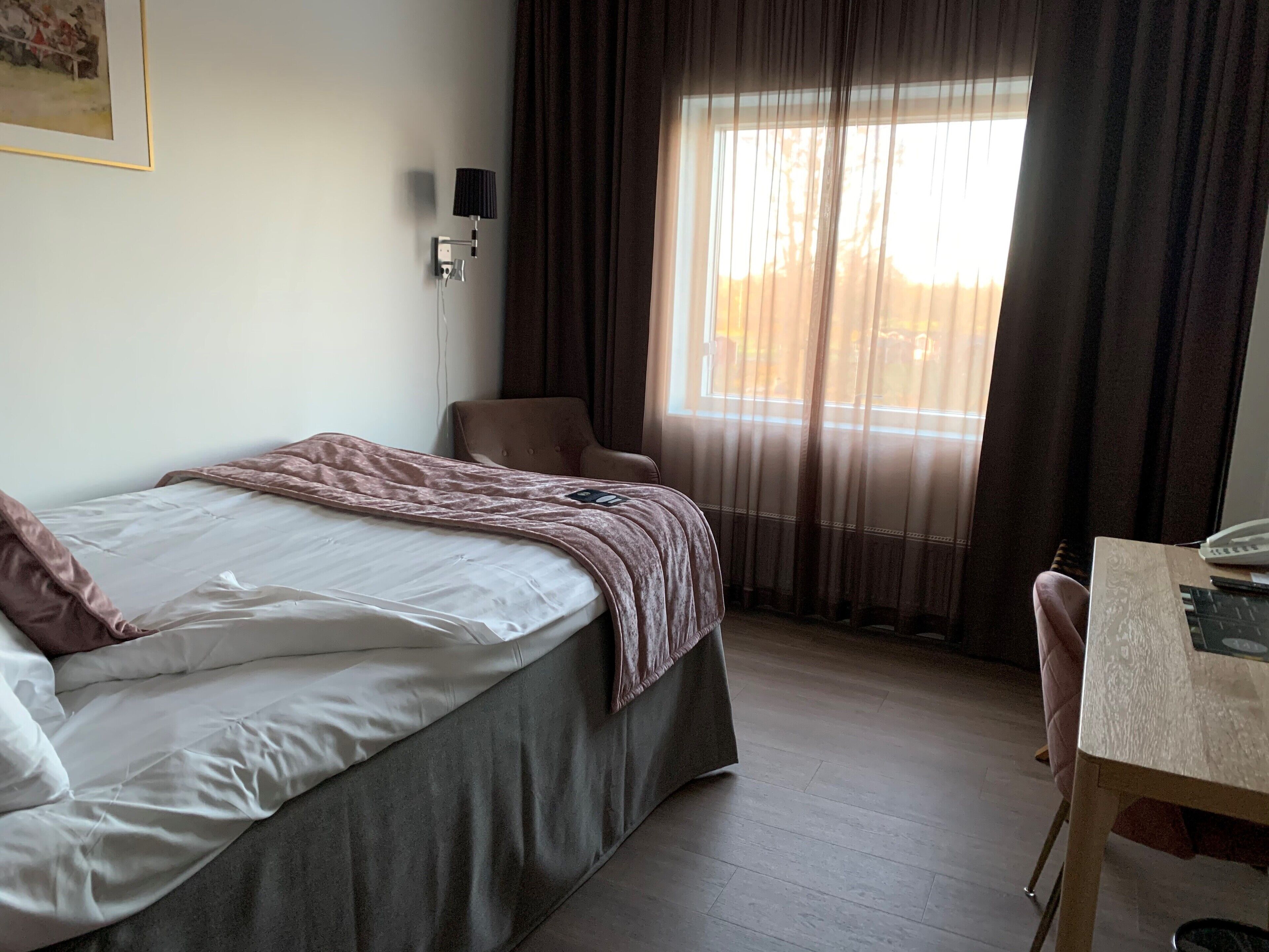 Una camera d'albergo con un letto, una sedia, una scrivania e una finestra con tende.