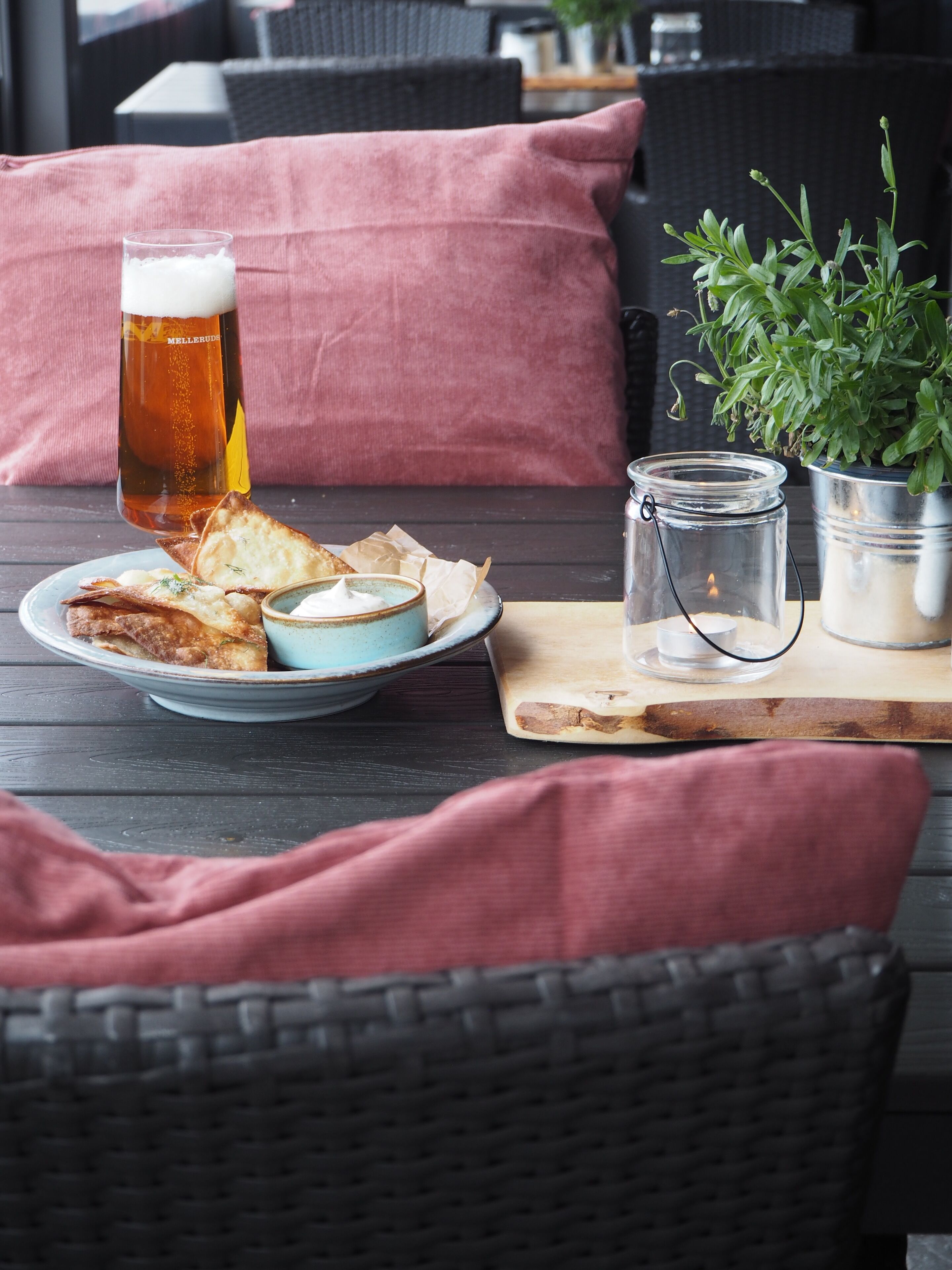 A dining table with a plate of food, a glass of beer, a jar of sauce, and a candle.