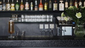 A bar with various bottles and glasses, a plant, and a vase with flowers. - Skara Konsthotell (Skara)