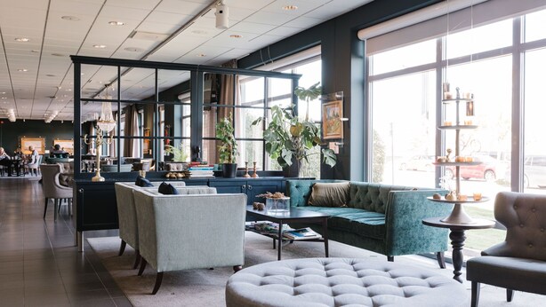 A modern lounge area with seating, large windows, and a view of the street. - Skara Konsthotell (Skara)
