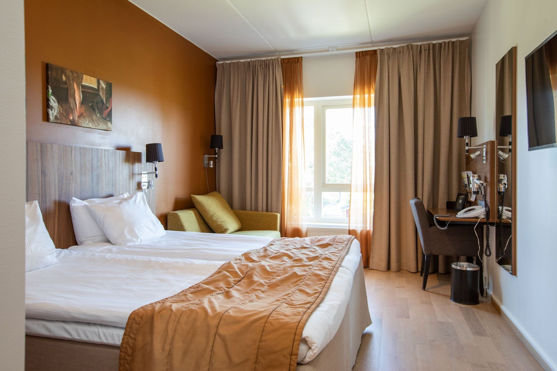 A hotel room with a large bed, a desk with a telephone, and a window with curtains.