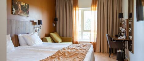 A hotel room with a large bed, a desk with a telephone, and a window with curtains.