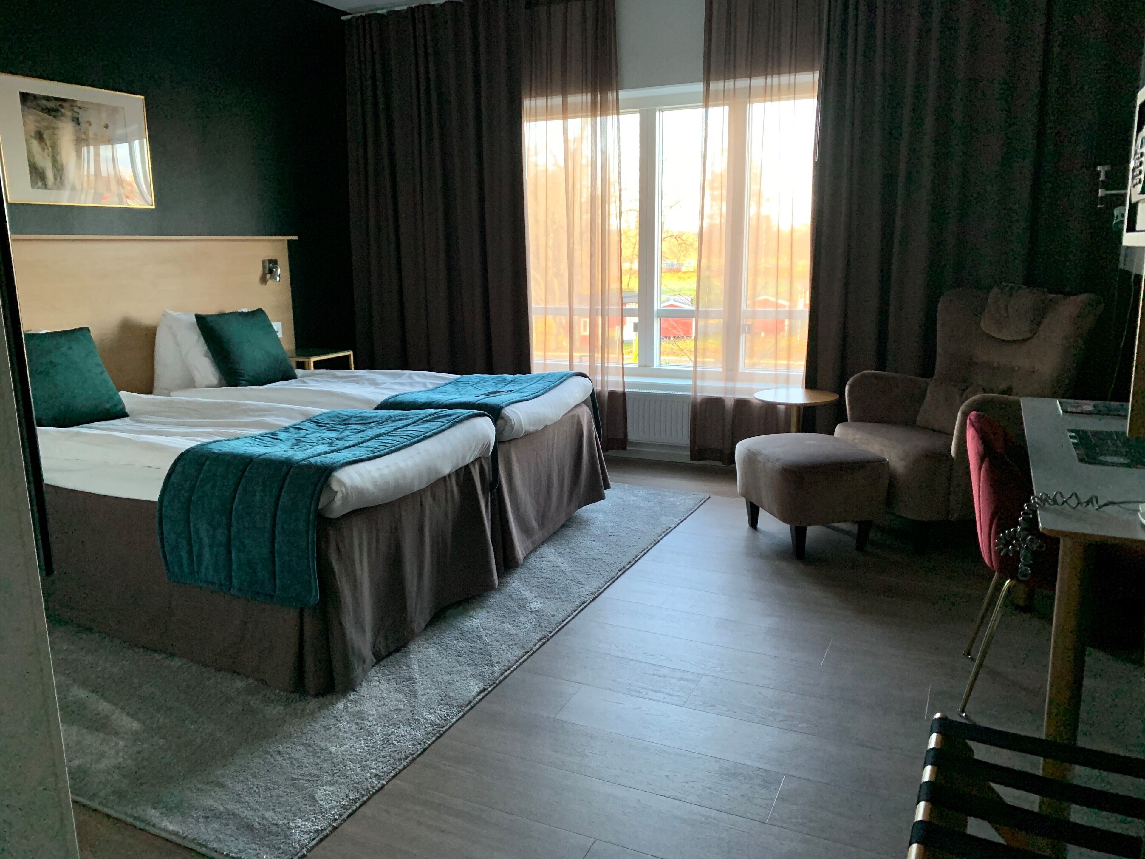 A hotel room with two beds, a chair, a small table, and a window with curtains.