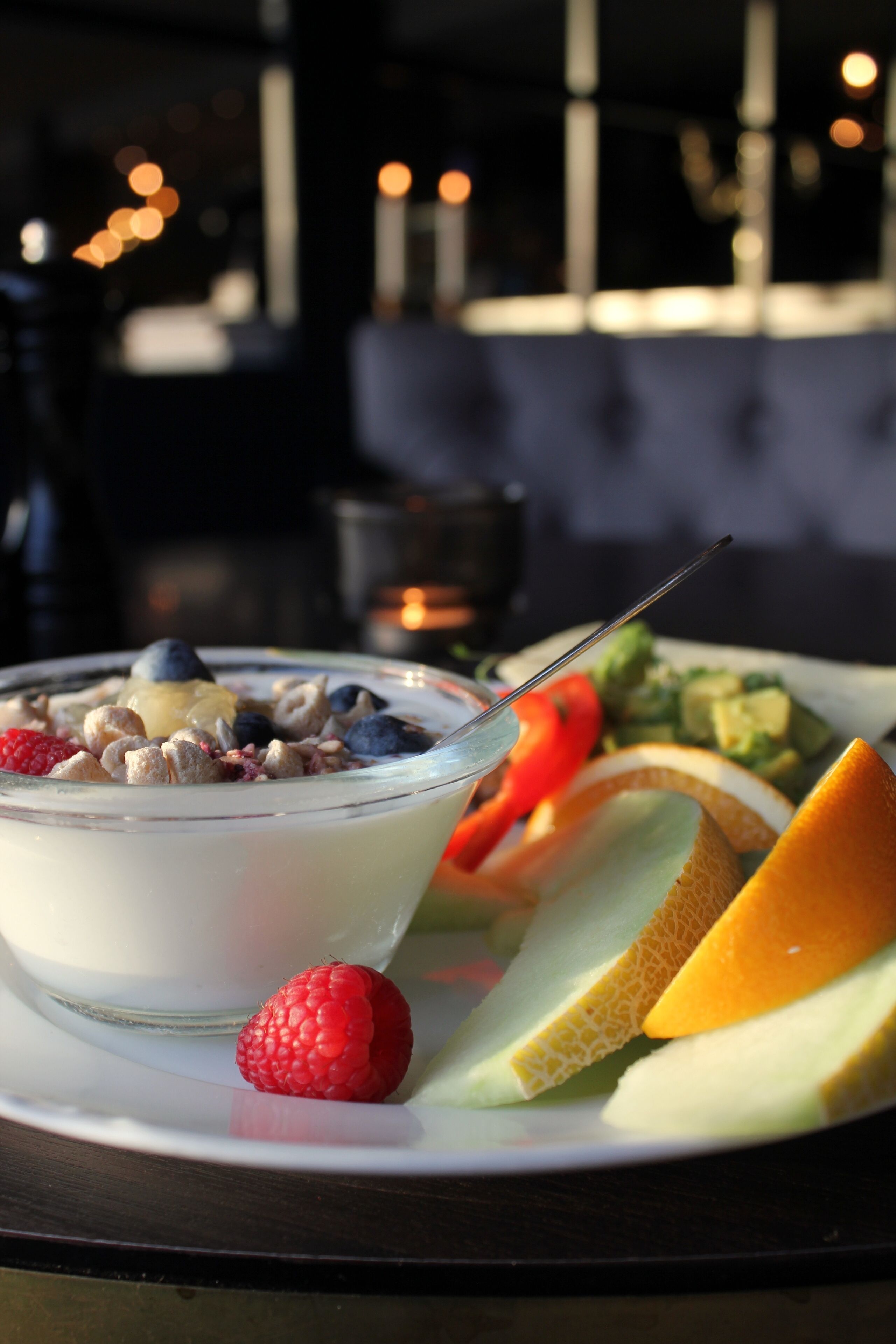 A bowl of yogurt with fruits and a plate of sliced melon and berries.