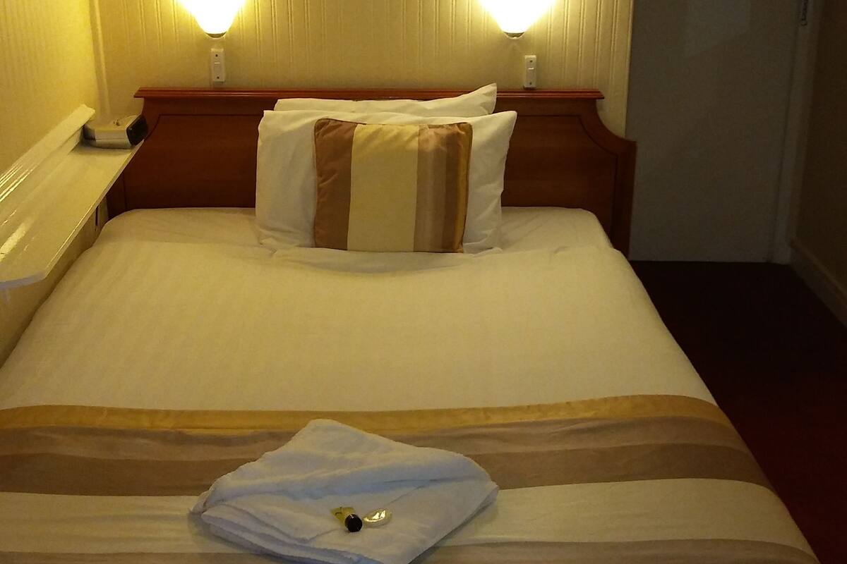A hotel room with a bed, two bedside lamps, a framed picture on the wall, and a door with a 'No Smoking' sign.