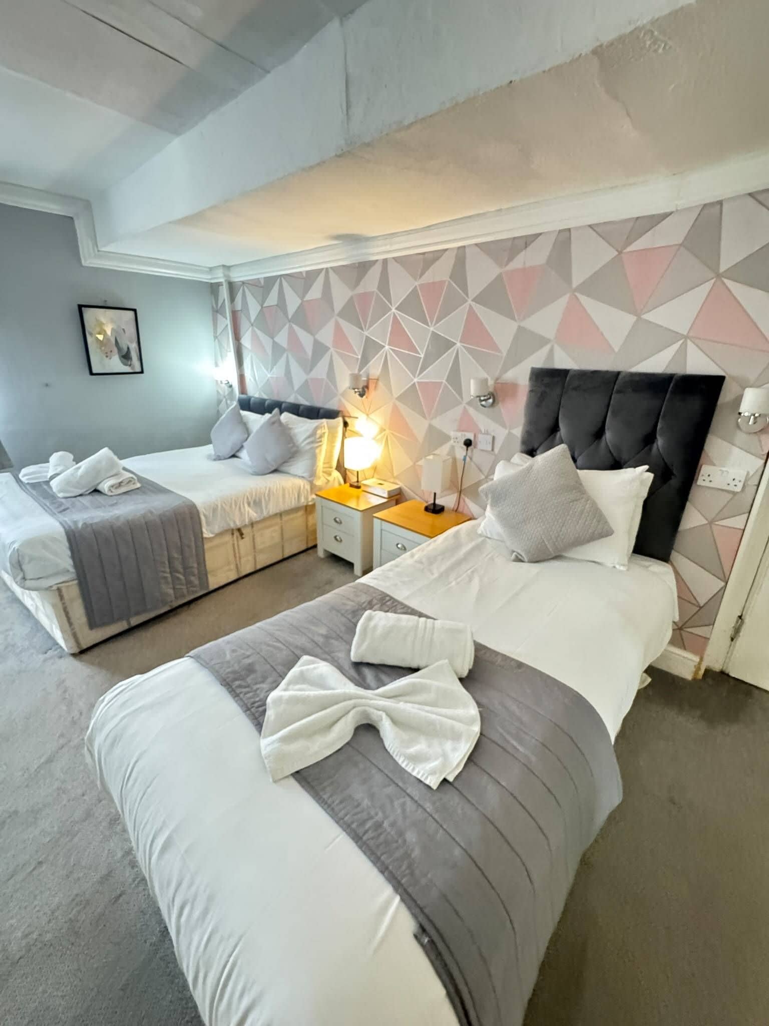 Camera d'albergo con due letti, una parete con motivo geometrico e un design moderno.