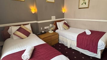 Habitación de hotel con dos camas, cada una con una manta roja y ropa blanca. Hay lámparas fijadas a la pared e impresiones botánicas enmarcadas.