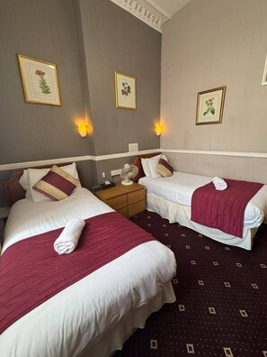 A hotel room with two beds, each with a red blanket and white linens. There are wall-mounted light fixtures and framed botanical prints on the walls. - Parkwood at Marble Arch (London)