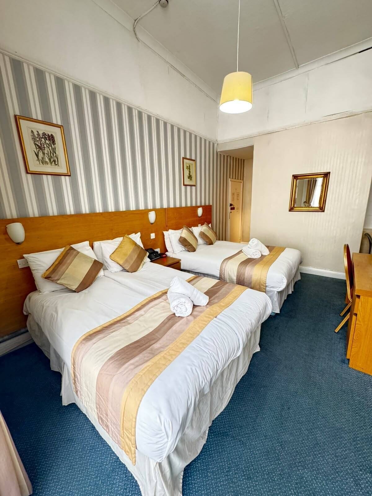 A hotel room with two beds, a wooden headboard, a desk, and a chair.