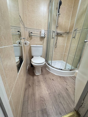 A bathroom with a toilet, a shower enclosure, and a toilet paper holder. - Parkwood at Marble Arch (London)
