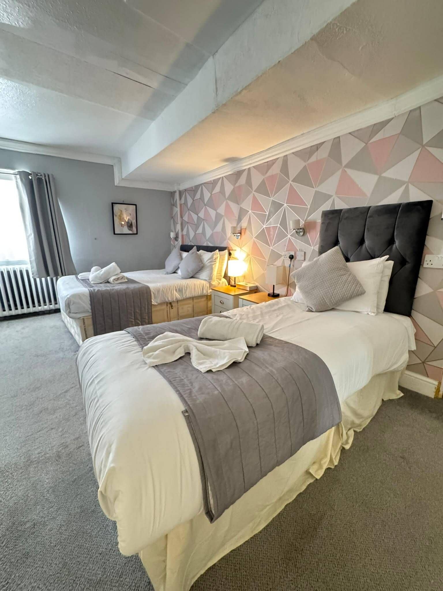 Een hotelkamer met twee bedden, een wand met een geometrisch patroon en een radiator.