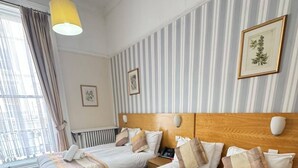A hotel room with two beds, striped wallpaper, a wooden headboard, a window with curtains, and a hanging light fixture. - Parkwood at Marble Arch (London)
