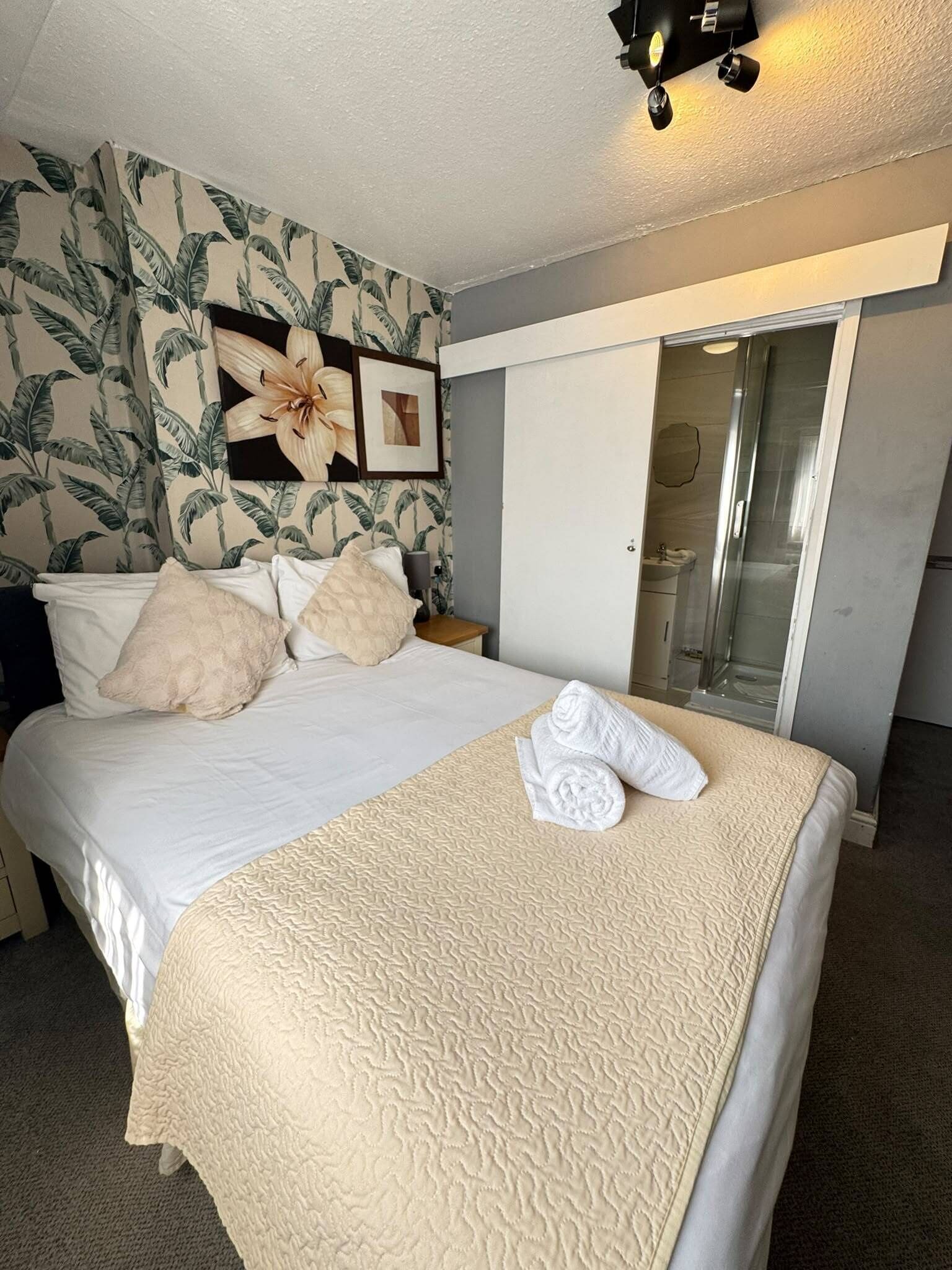 A hotel room with a bed, a shower, and a bathroom with a glass door.