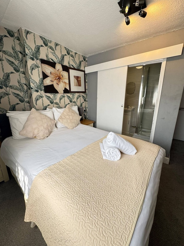 A hotel room with a bed, a shower, and a bathroom with a glass door. - Parkwood at Marble Arch (London)