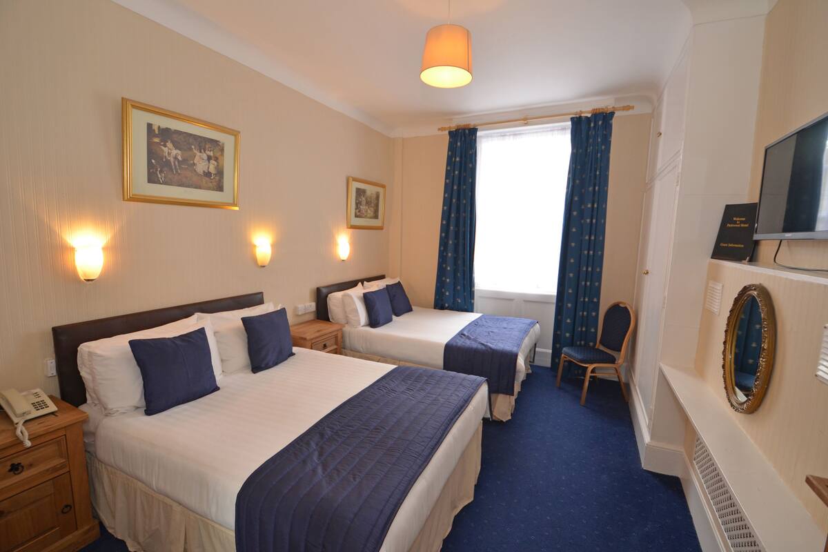 A hotel room with two beds, a television, a mirror, and a window with curtains.