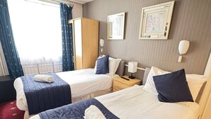 A hotel room with two beds, a wardrobe, a bedside table with a lamp, and a window with curtains. - Parkwood at Marble Arch (London)