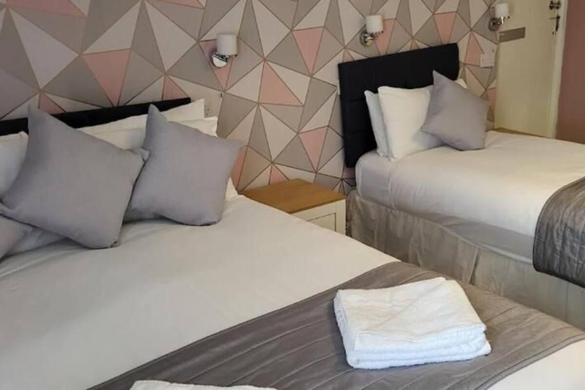 Two beds with grey bedding and pillows, a wooden nightstand, and a wall with geometric patterns.