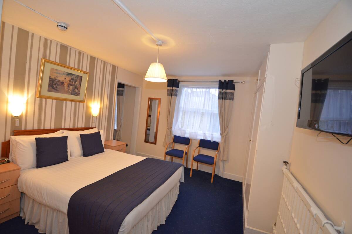 A hotel room with a large bed, bedside tables, a desk with two chairs, a television, and a window with curtains.