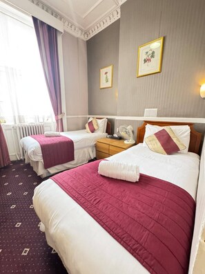 A hotel room with two beds, a nightstand, a radiator, and a window with curtains. - Parkwood at Marble Arch (London)