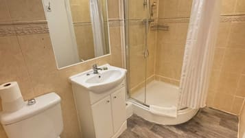 Un baño con inodoro, lavamanos y ducha con mampara de vidrio.