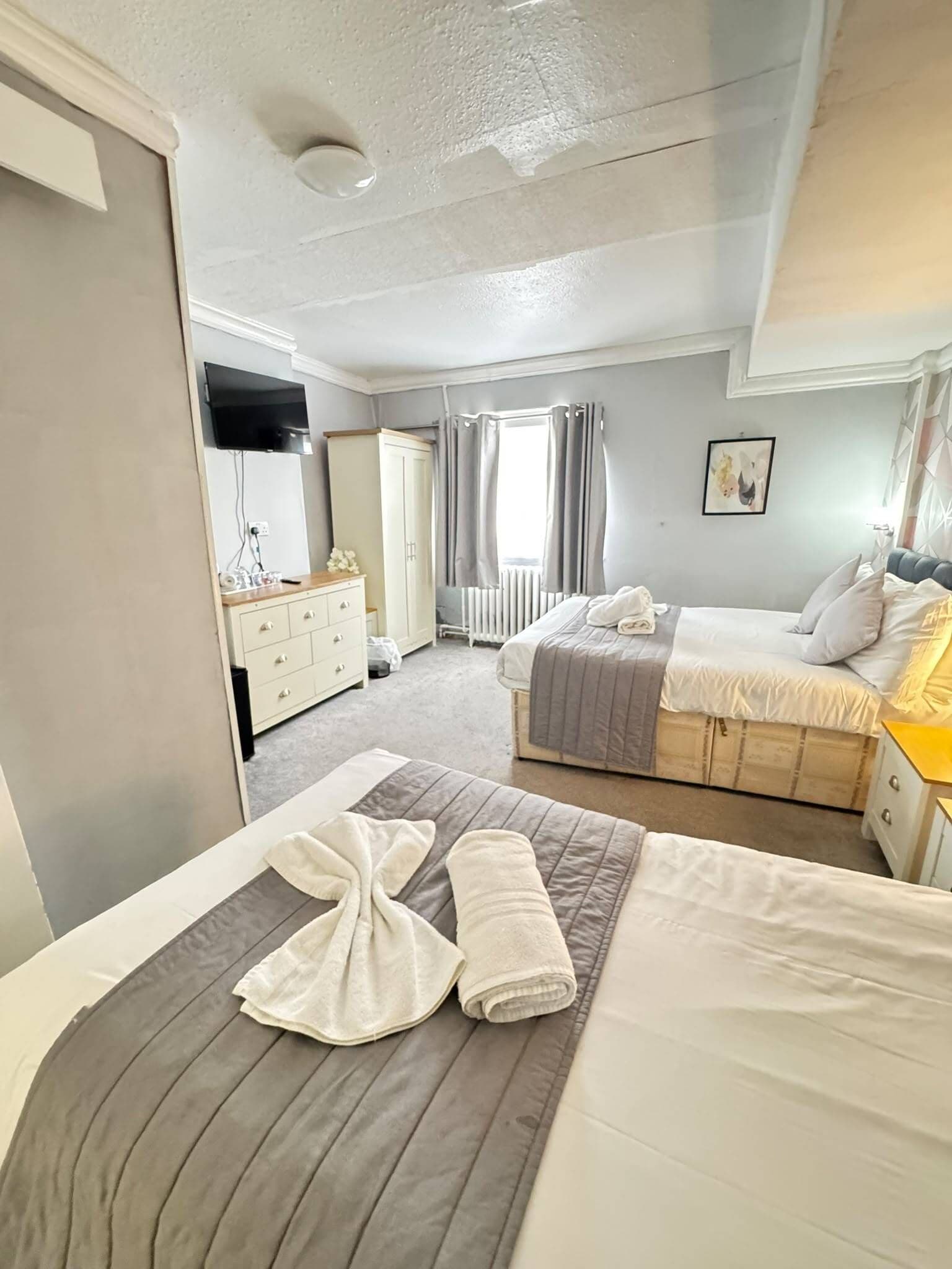 A hotel room with a bed, a bedside table, a wardrobe, and a window with curtains.