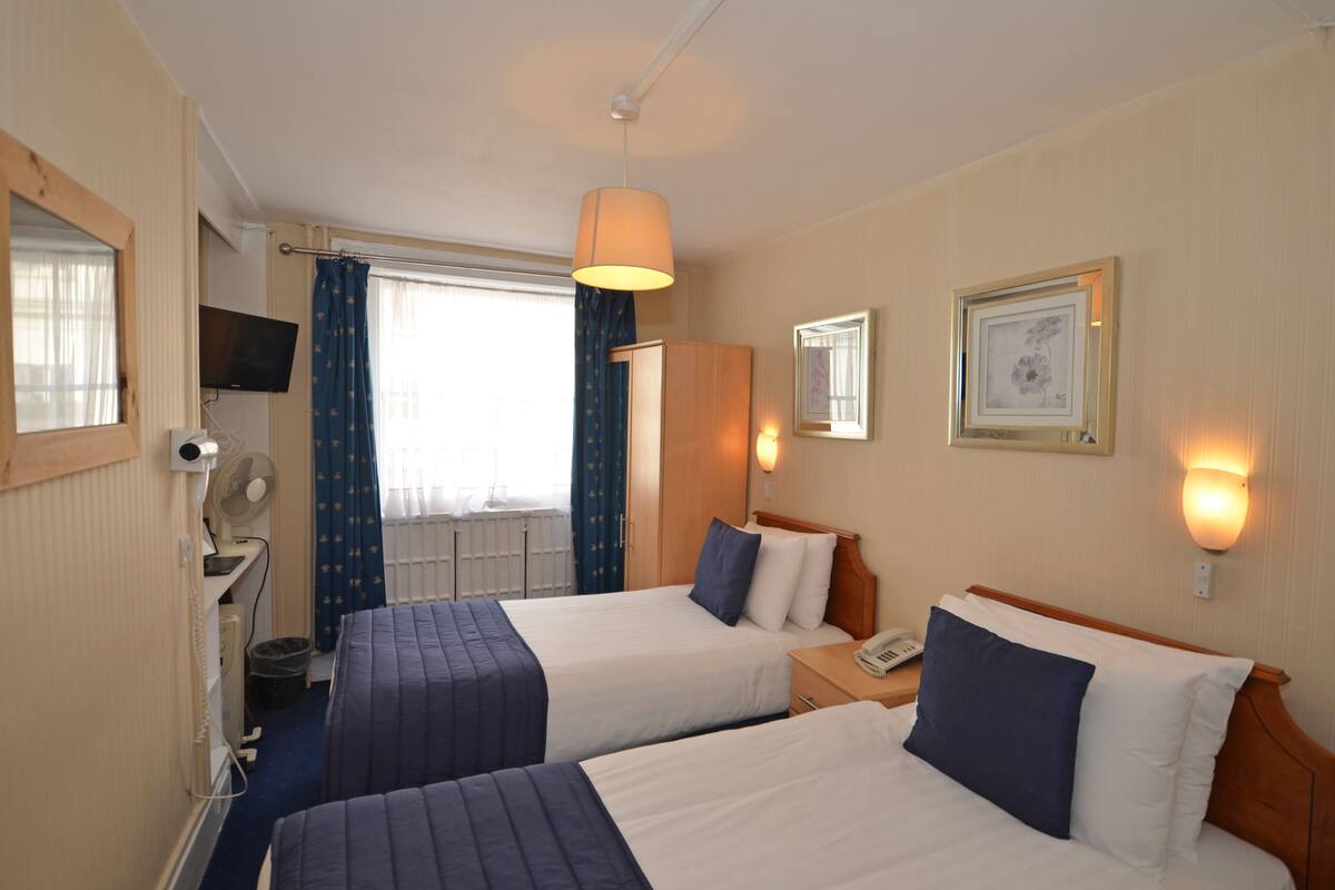 A hotel room with two beds, a desk, a chair, a TV, and a window with curtains.
