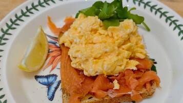Sándwich con huevos revueltos y salmón ahumado sobre una rebanada de pan, acompañado de una rodaja de limón y algunas verduras en un plato decorativo.