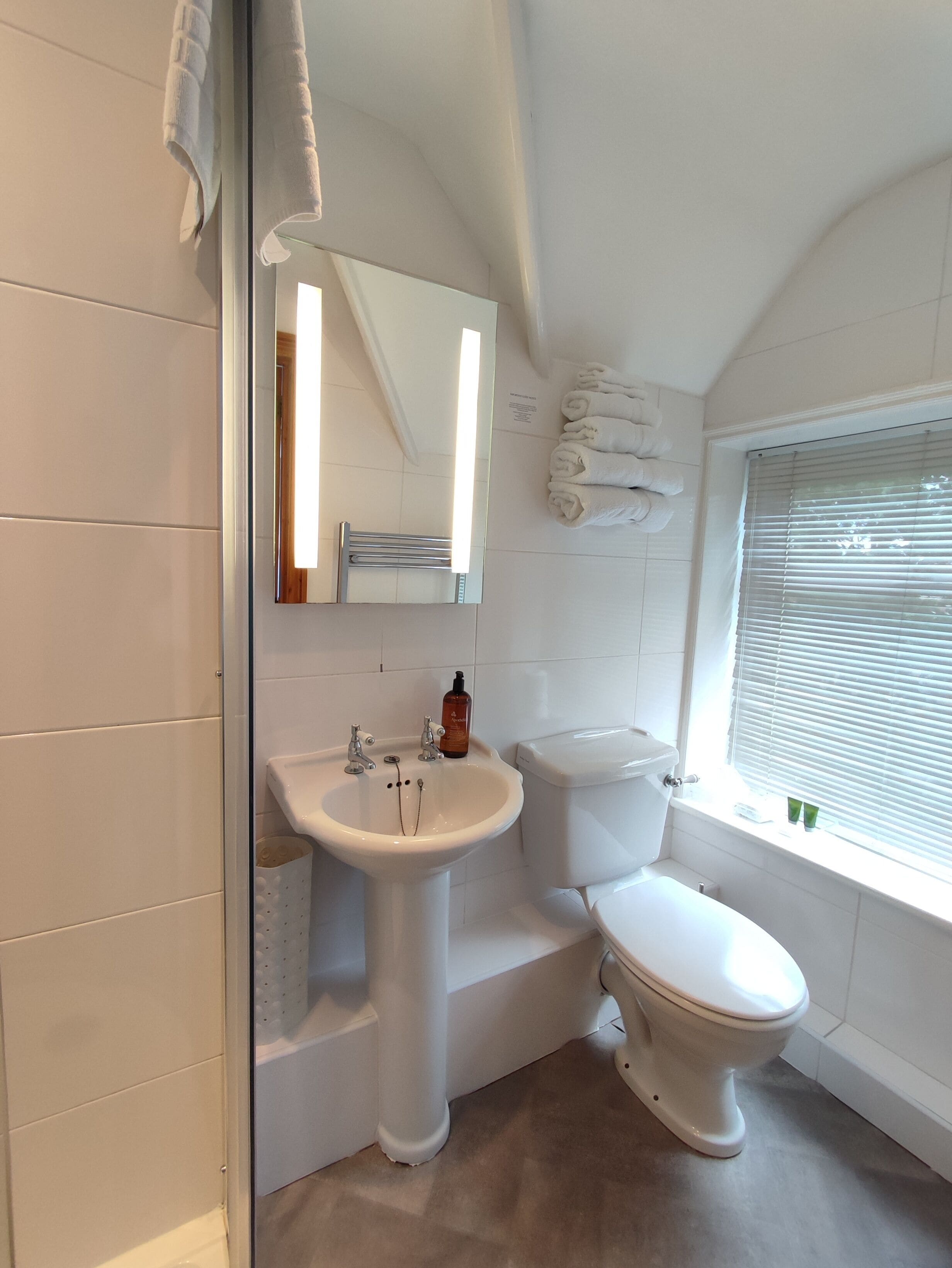 Un baño con un lavamanos blanco, un inodoro y una ventana con persianas.