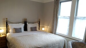 Un lit bien fait, recouvert d’une couvre-lit à motifs, une table de chevet avec une lampe et une fenêtre avec des rideaux.