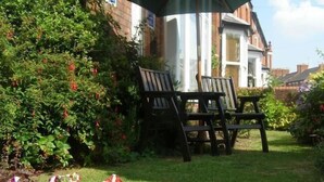 Un jardin avec un banc en bois et une maison en arrière-plan.