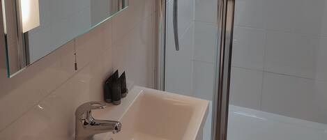 Un baño con lavamanos, espejo y cabina de ducha de vidrio.