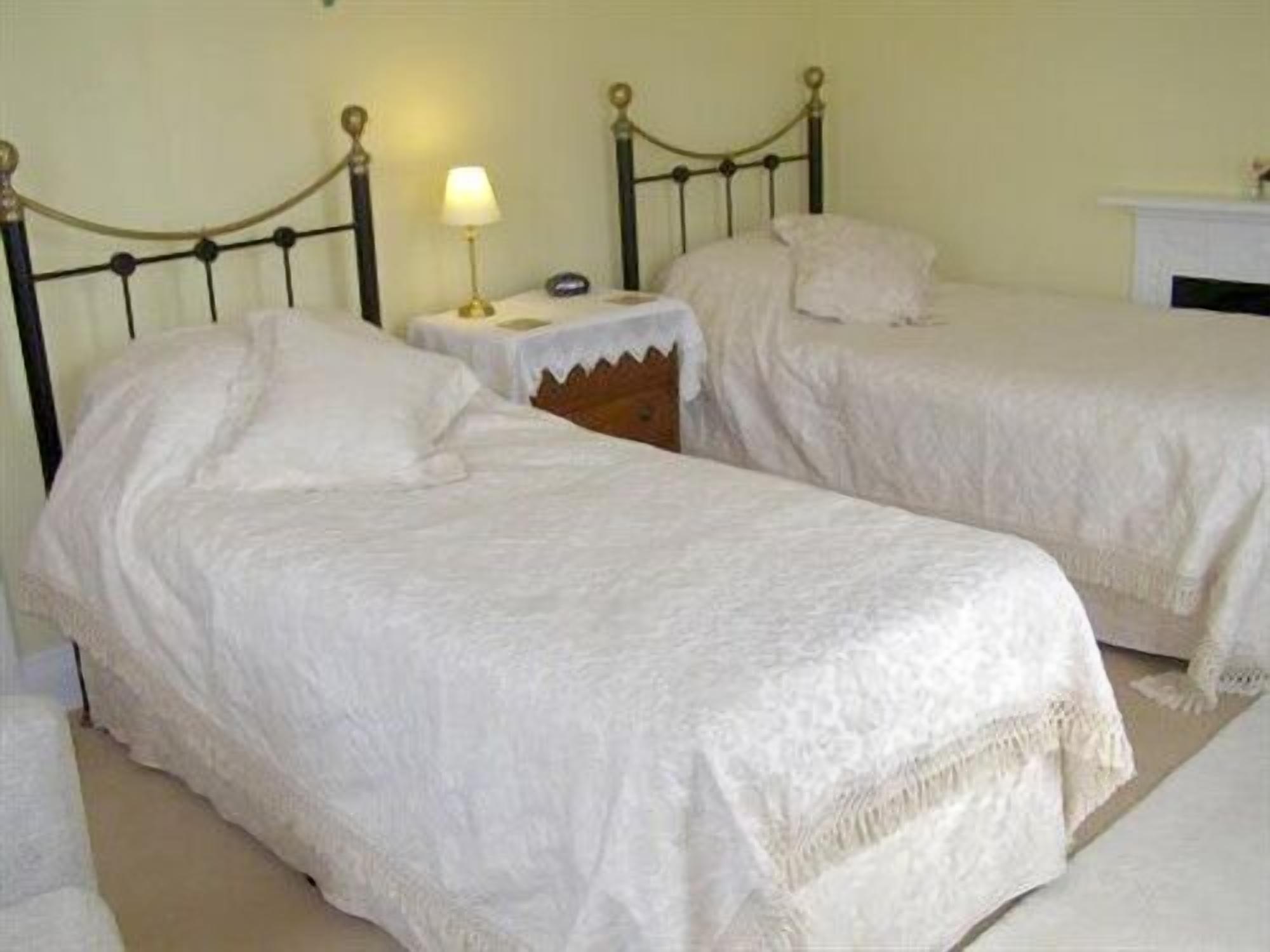 Quarto com duas camas de solteiro, mesa de cabeceira com abajur e criado-mudo pequeno.