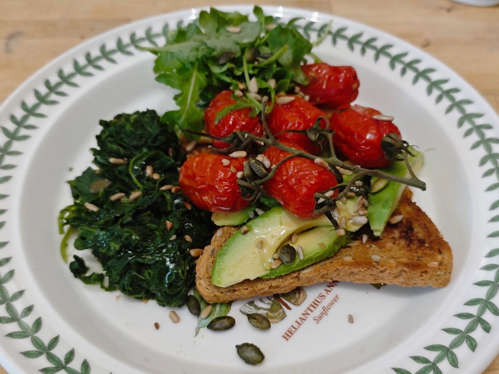 Un plato con un sándwich, vegetales verdes y tomates cherry.