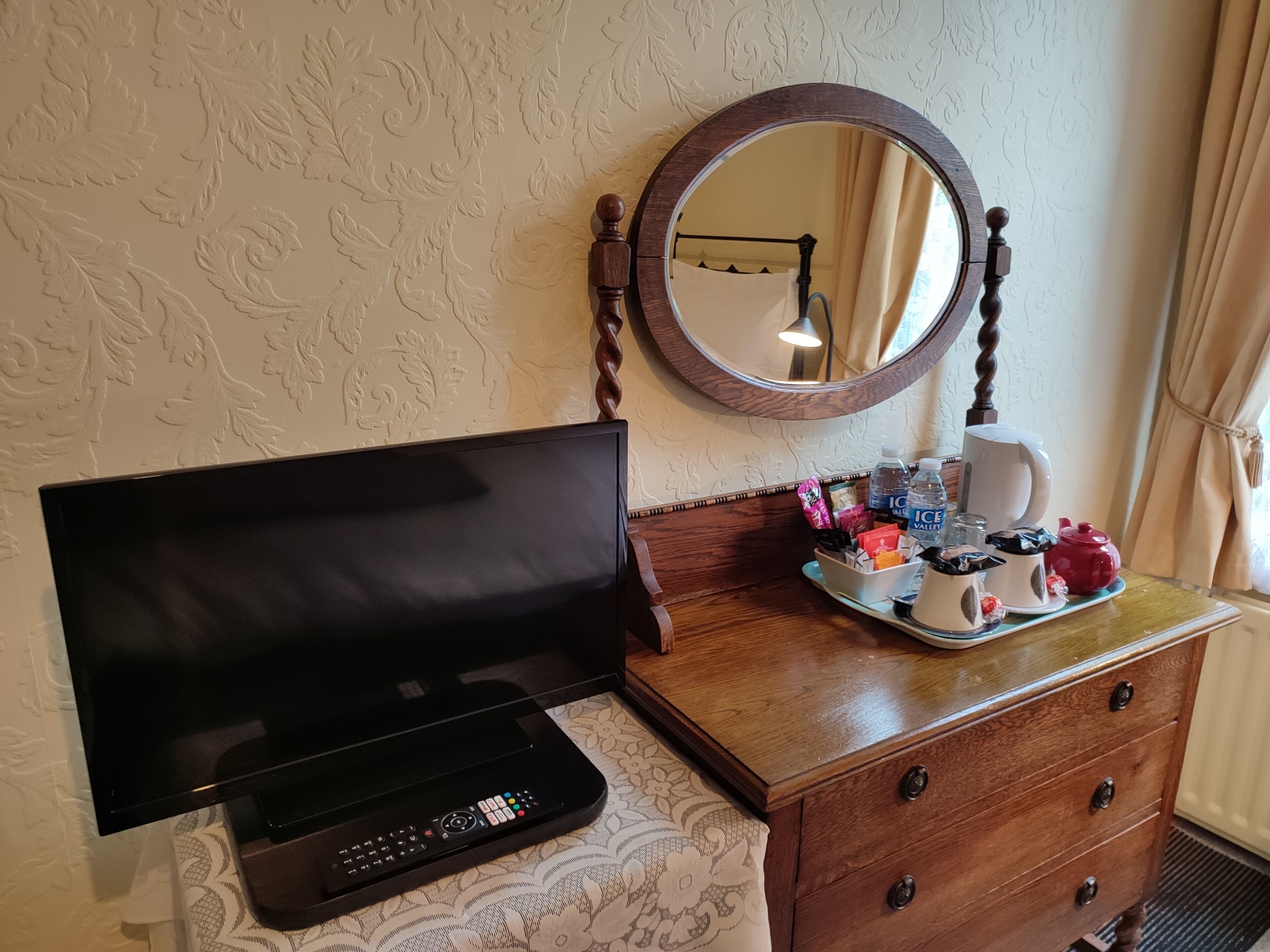 Une chambre d’hôtel équipée d’un téléviseur à écran plat, d’une commode en bois, d’un miroir et d’un plateau avec des articles de toilette.
