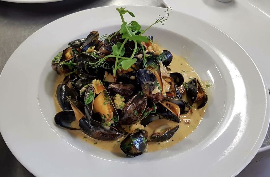 A plate of mussels in a creamy sauce, garnished with herbs.