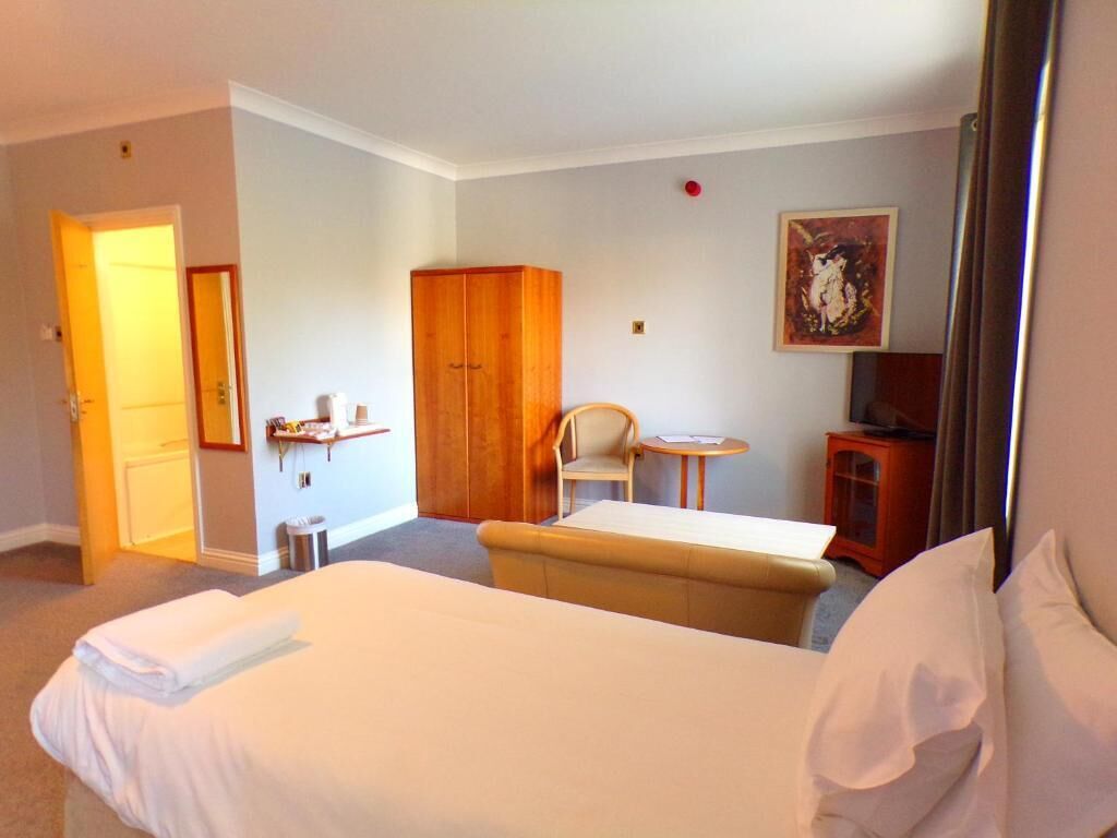 Una camera d'albergo con un letto, una sedia, un tavolino, un armadio e un quadro appeso al muro.