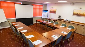 Un salón de conferencias con una larga mesa, sillas, una pantalla de proyector, una pizarra y un área de café.