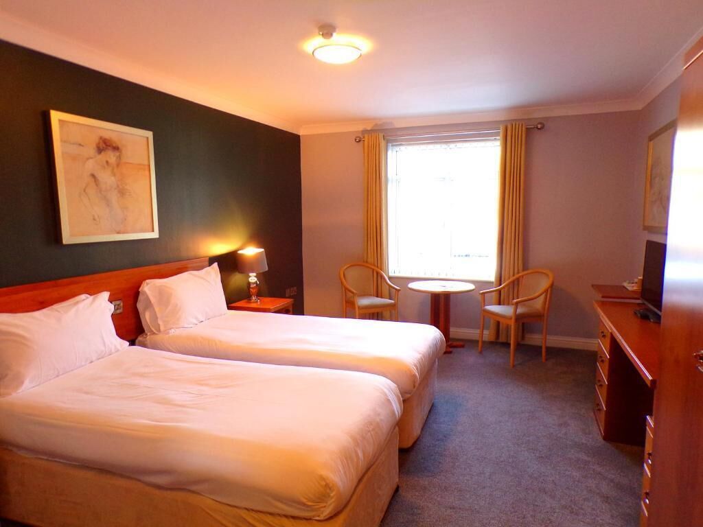 Habitación de hotel con dos camas, un escritorio, una silla, una mesita y una ventana con cortinas.