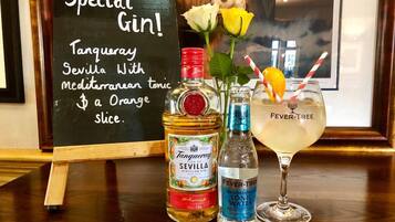 A bar setup with a special gin cocktail, a bottle of Seville Tanqueray, a bottle of Fever-Tree tonic water, and a glass with an orange slice.