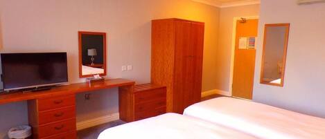 A hotel room with a bed, a desk with a television, a wardrobe, and a mirror.